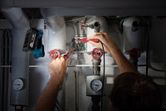 Person checking electrical wires near pipes, cordless work light attached above.