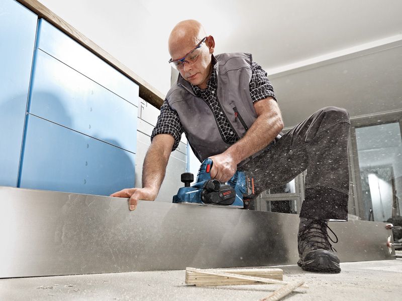 GHO 18V-LI A person wearing safety equipment planes a wooden board using a cordless planer.