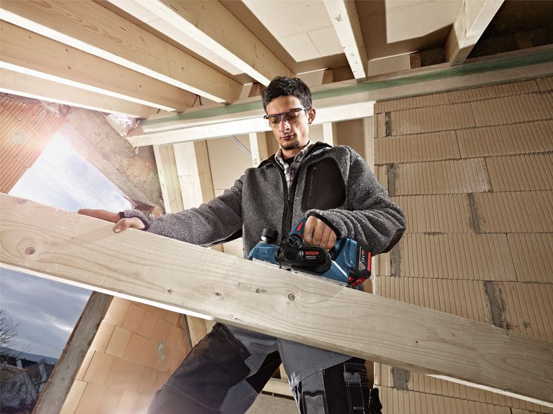 GHO 18V-LI A person wearing safety equipment uses a cordless planer on a wooden beam.