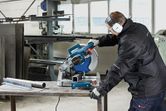A person wearing safety equipment cuts a metal pipe with a metal cut-off saw.