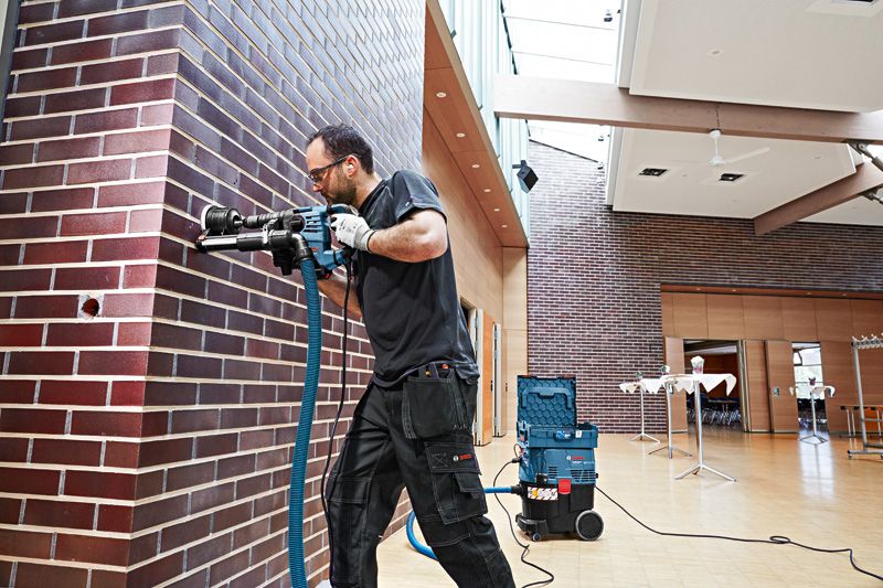 A person wearing safety equipment drills into a brick wall using a system accessory tool.