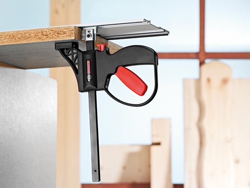 System accessory clamp securing a wooden board to a metal surface in a workshop.