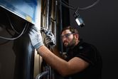 A person wearing safety equipment drills into a wall, cordless light illuminating the workspace.