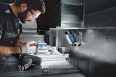 A person wearing safety equipment works with electrical wiring under a cordless work light.