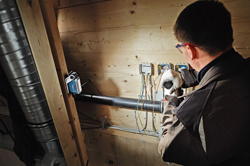 GLI 12V-330 A person wearing safety equipment works on electrical wiring under bright cordless light.