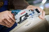 A person trims a wooden board using a cordless circular saw.