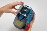 A person opens the base plate of a blue handheld power tool.