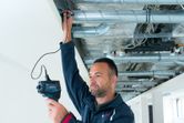 A person uses a thermo detector to inspect HVAC pipes on a ceiling.