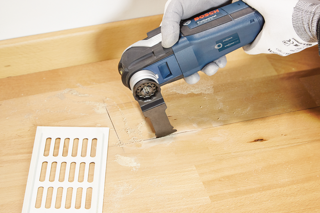 HCS plunge cut saw blade AIZ 32 BSPC Hard Wood Worker wearing safety equipment uses a multitool to cut a vent opening in wooden flooring.