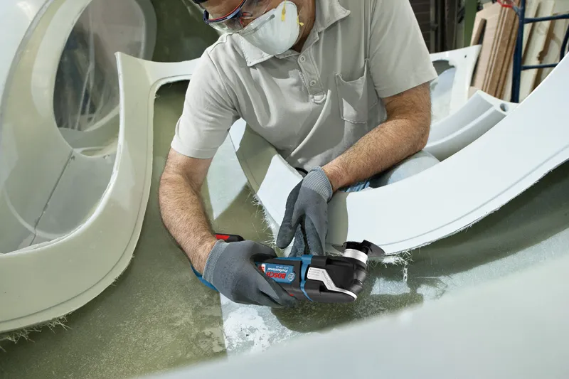 GOP 18V-28 A person wearing safety equipment cuts fiberglass with a cordless multi-tool.