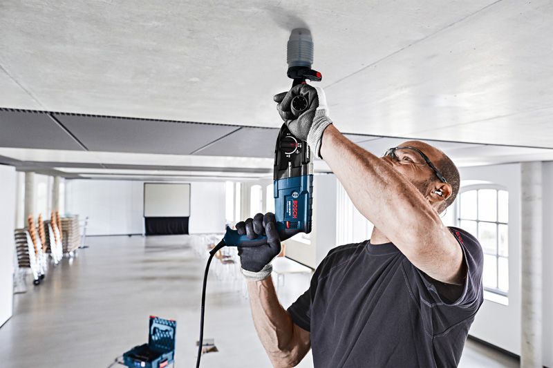 Dust Attachment A person wearing safety equipment drills into a ceiling with a dust collection cover attached.