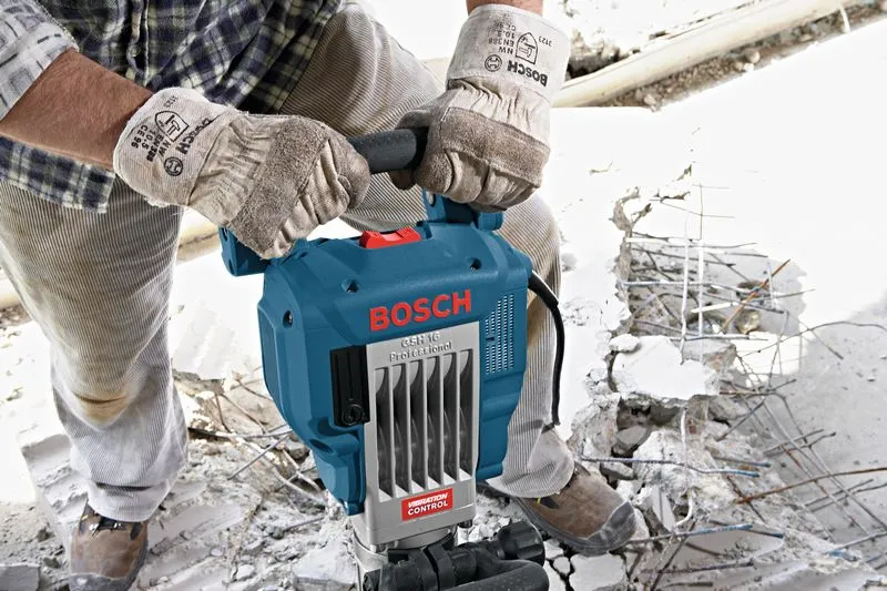 A person wearing safety equipment operates a demolition hammer to break concrete.
