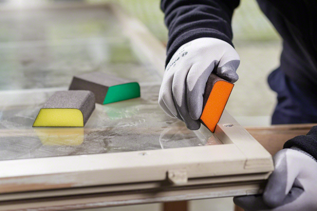 Foam abrasives std pad -M Worker wearing safety equipment sanding a window frame with a sanding sponge.