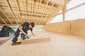 A person wearing safety equipment cuts plywood sheets with a cordless circular saw.