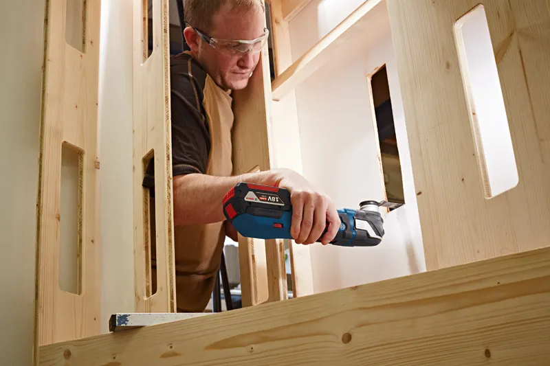 GOP 18V-28 A person wearing safety equipment cuts a wooden board with a cordless multi-tool.