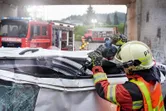 A person wearing safety equipment uses a power saw to cut a damaged vehicle roof.