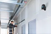 Person wearing safety equipment uses a drill to install a metal frame aligned with a laser leveling tool.