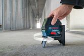 A person adjusts a laser leveling tool on a concrete floor in an unfinished hallway.