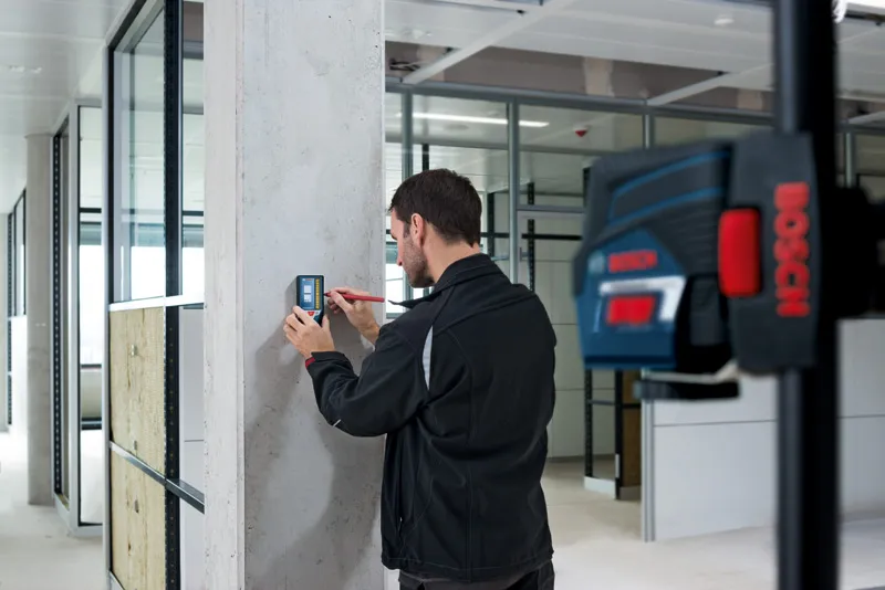 Person marking a wall using a laser receiver in an office interior.