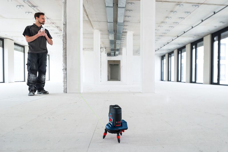 RM 3 A person stands in a large empty room while a laser leveling tool accessory projects a green line.