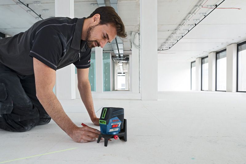 GCL 2-50 CG A person marks a line on the floor using a laser leveling tool in a large empty room.