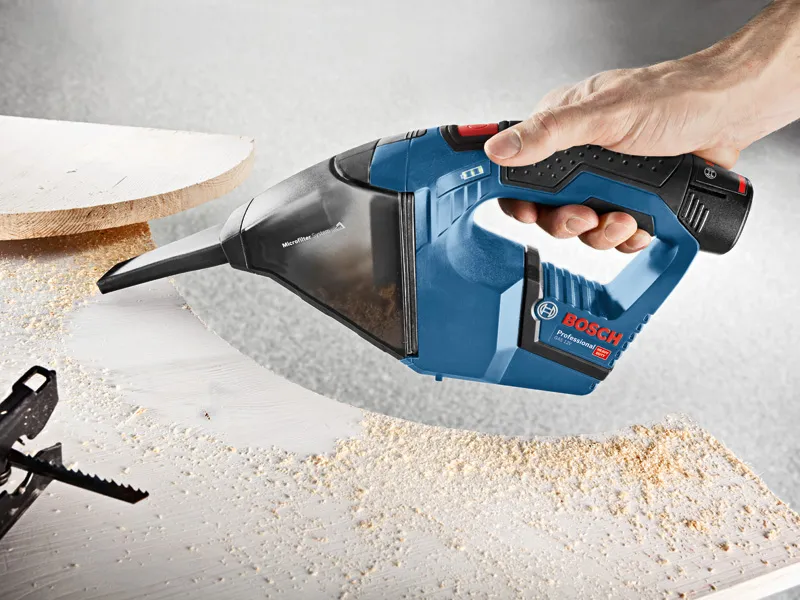 GAS 12 V-LI Person using a cordless vacuum cleaner to remove sawdust from a wooden surface.