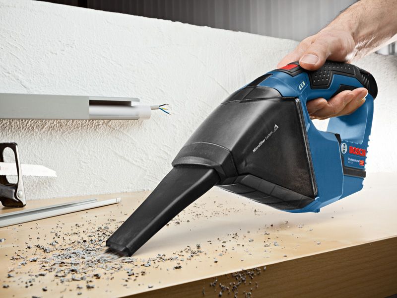 GAS 12 V-LI A person uses a cordless vacuum cleaner to pick up debris from a workbench.