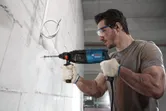 A person wearing safety equipment drills into a concrete wall with a power tool.