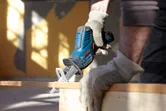 A person wearing safety equipment uses a cordless reciprocating saw to cut wood.