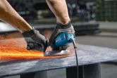 A person wearing safety equipment grinds metal, creating sparks with an angle grinder.