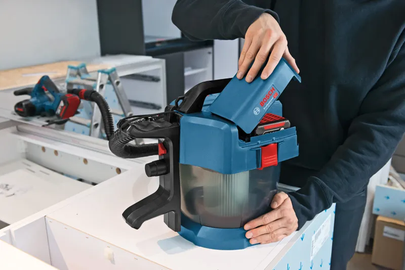 Person inserts a battery into a cordless dust extractor on a workbench.