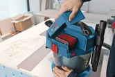 A person inserts a battery into a cordless dust extractor on a workbench.