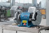 Double-wheeled bench grinder placed on a metal workbench in an industrial workshop.