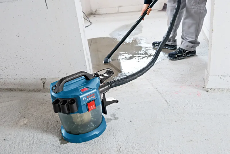 A person uses a cordless dust extractor to clean liquid from a concrete floor.