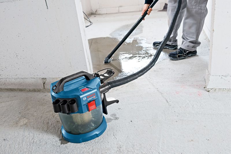 A person uses a cordless dust extractor to clean liquid from a concrete floor.