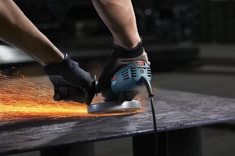 A person wearing safety equipment grinds metal, producing bright sparks.