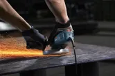 A person wearing safety equipment grinds metal, producing bright sparks.