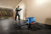 A person wearing safety equipment drills into a wall, connected to a wet dry extractor.