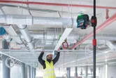 A person wearing safety equipment aligns a ceiling frame using a laser leveling tool.