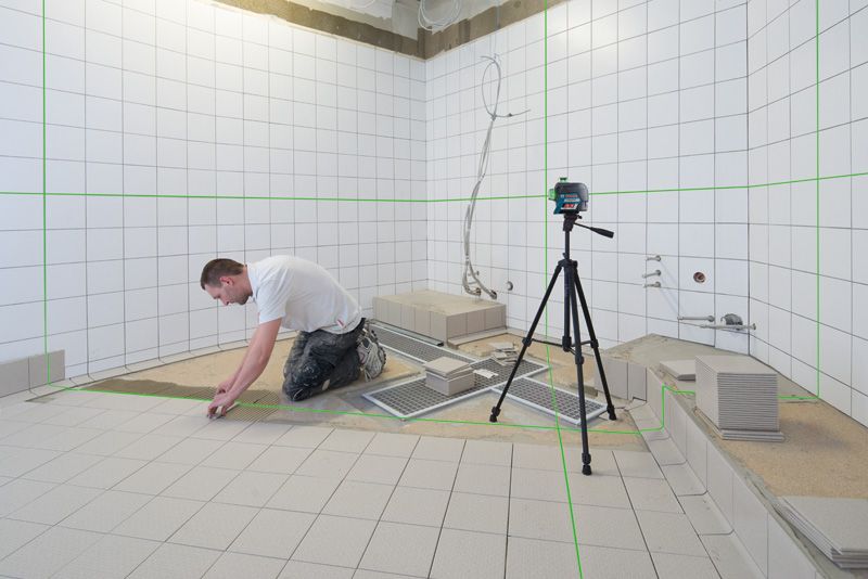 GLL 3-80 CG Person installing tiles in a bathroom, using a laser leveling tool on a tripod.