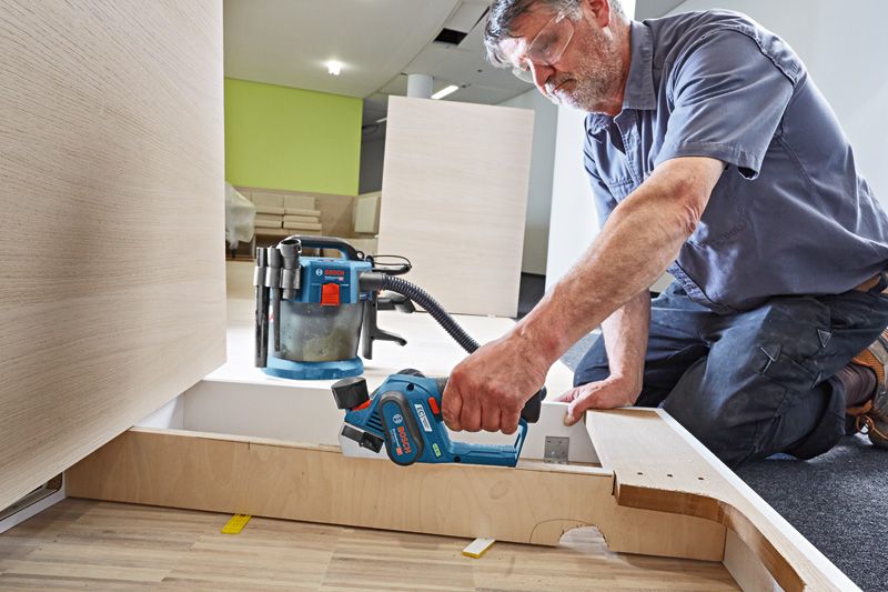 GHO 12V-20 A person wearing safety equipment uses a cordless planer to smooth wooden panels.