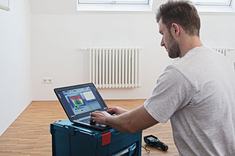 GTC 400 C Person analyzing thermal camera data on a laptop in a room with a radiator.