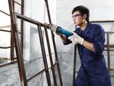 A person wearing safety equipment grinds a metal window frame with a straight grinder.