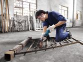 A person wearing safety equipment grinds metal scrollwork inside a workshop.