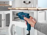 A person drills a hole in a wooden drawer with a blue electric drill.