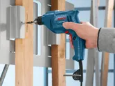 A person drills into a wooden beam mounted in a metal frame.