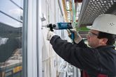 A person wearing safety equipment drills into a concrete wall on a construction site.