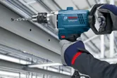 A person wearing safety equipment drills into a metal beam with a power tool.