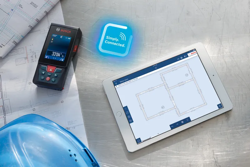 GLM 150 C Laser measure on blueprints beside a digital tablet displaying building plans.