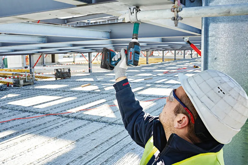 ProCORE18V 4.0Ah A person wearing safety equipment uses a cordless impact wrench on a metal beam.